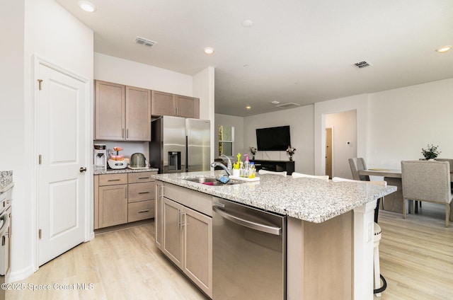 kitchen featuring sink, an island with sink, a breakfast bar area, appliances with stainless steel finishes, and light wood-type flooring