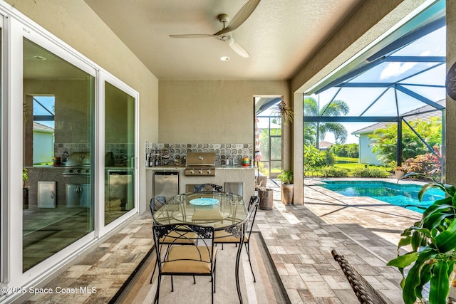 exterior space featuring ceiling fan, glass enclosure, area for grilling, and exterior kitchen