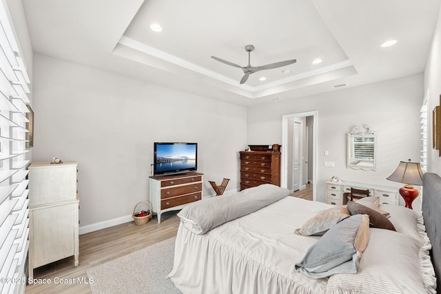 bedroom featuring ceiling fan, a tray ceiling, and light wood-type flooring