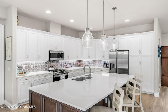 kitchen with decorative light fixtures, stainless steel appliances, a center island with sink, white cabinets, and sink