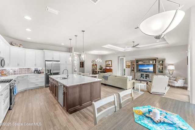 kitchen with a raised ceiling, a kitchen island with sink, white cabinets, appliances with stainless steel finishes, and sink