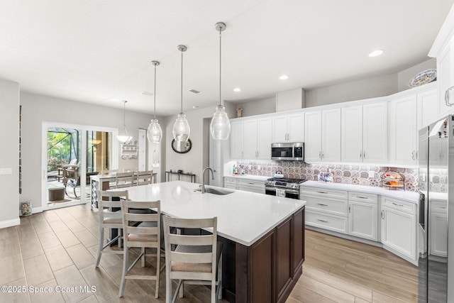 kitchen with a kitchen breakfast bar, a kitchen island with sink, stainless steel appliances, hanging light fixtures, and white cabinets