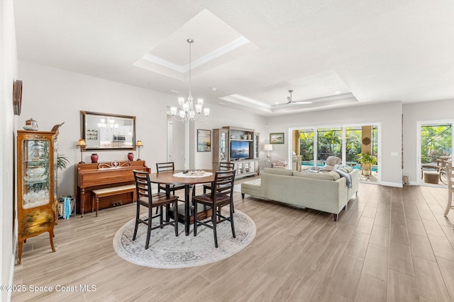 dining room featuring ceiling fan with notable chandelier, a raised ceiling, light hardwood / wood-style floors, and a healthy amount of sunlight