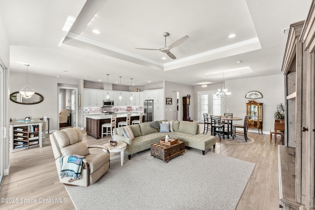 living room with ceiling fan with notable chandelier, a raised ceiling, light wood-type flooring, and crown molding