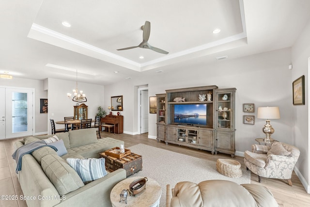 living room featuring ceiling fan with notable chandelier, light wood-type flooring, french doors, and a tray ceiling