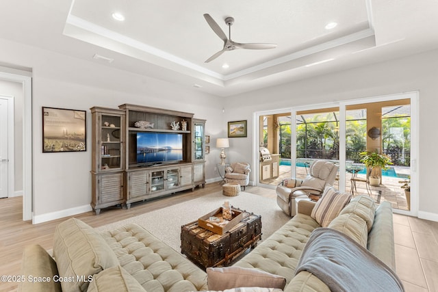 living room with a raised ceiling, ceiling fan, and light wood-type flooring