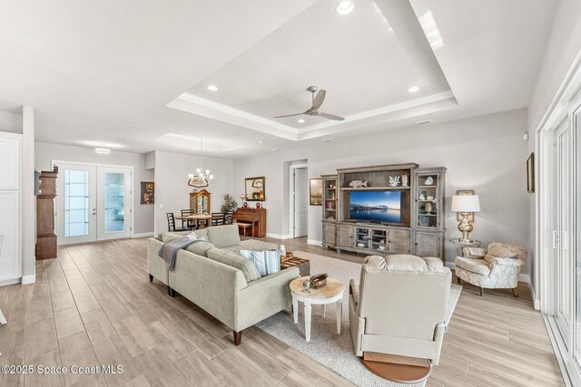 living room featuring french doors, ceiling fan with notable chandelier, and a tray ceiling