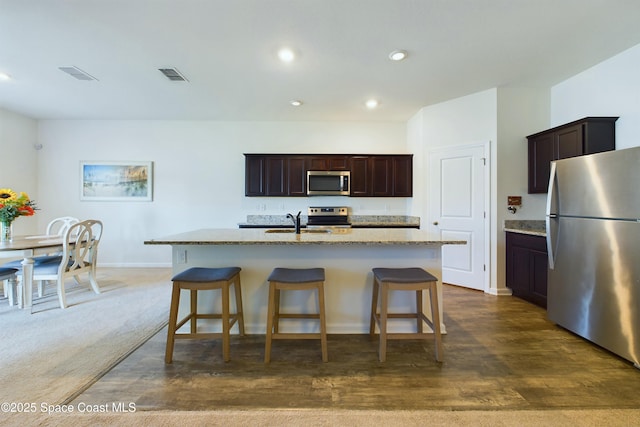 kitchen featuring sink, a breakfast bar, stainless steel appliances, light stone counters, and an island with sink