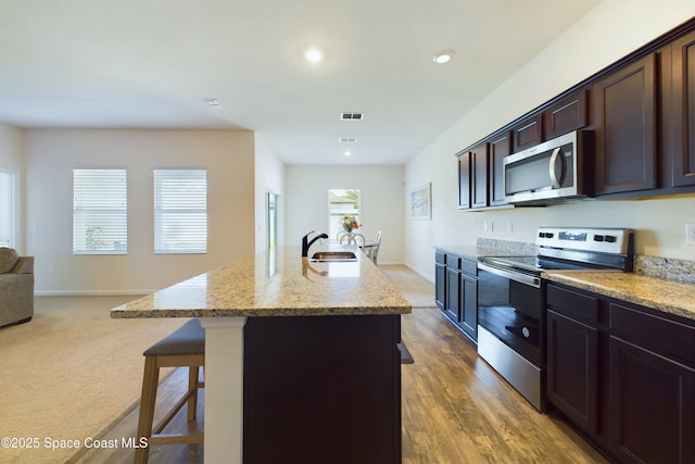 kitchen featuring sink, a breakfast bar area, light stone counters, stainless steel appliances, and a kitchen island with sink