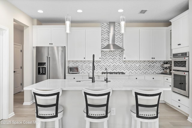 kitchen featuring decorative light fixtures, a kitchen bar, wall chimney range hood, and appliances with stainless steel finishes