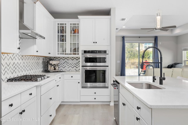 kitchen with sink, wall chimney exhaust hood, tasteful backsplash, white cabinetry, and stainless steel appliances