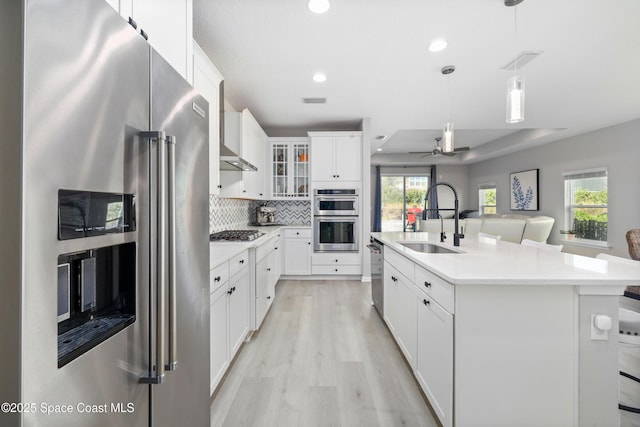 kitchen with sink, stainless steel appliances, backsplash, decorative light fixtures, and a kitchen island with sink