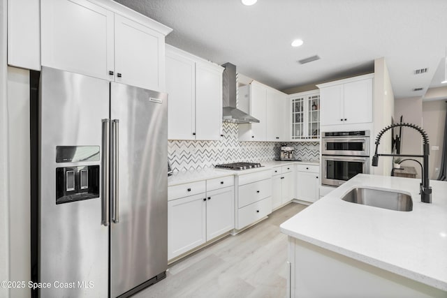 kitchen with appliances with stainless steel finishes, sink, white cabinetry, and wall chimney range hood