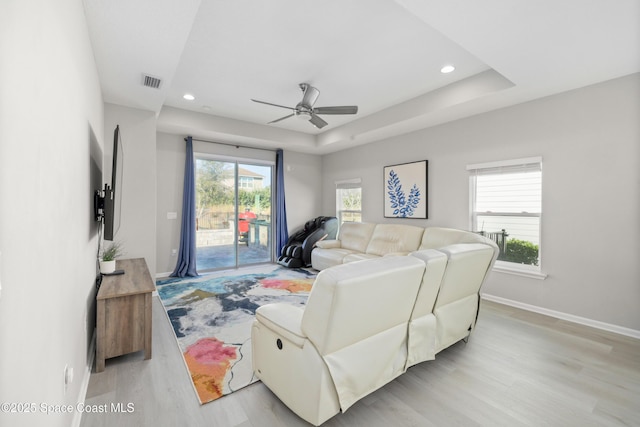 living room featuring ceiling fan, a raised ceiling, and light wood-type flooring