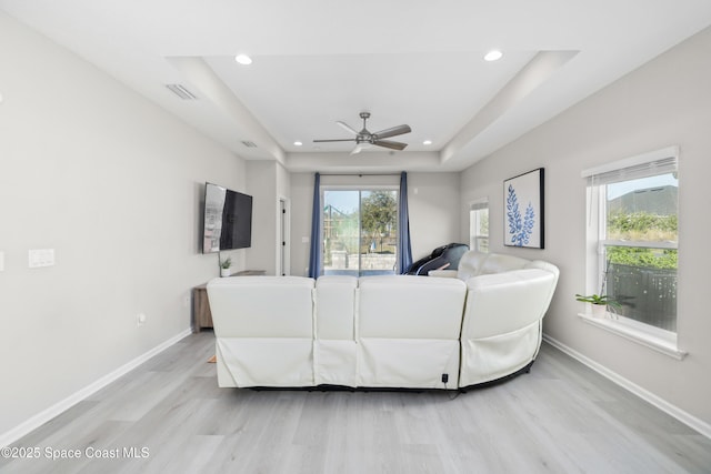 living room featuring a raised ceiling, ceiling fan, and light wood-type flooring