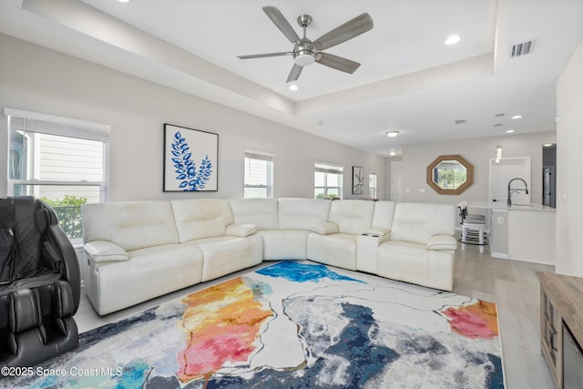 living room featuring a tray ceiling, a wealth of natural light, and light wood-type flooring