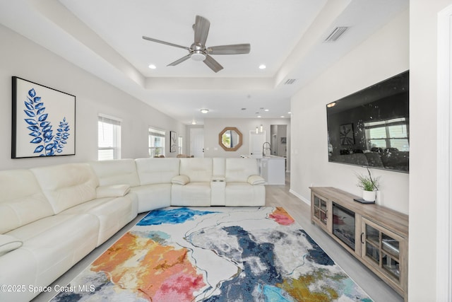 living room with a tray ceiling, ceiling fan, sink, and light hardwood / wood-style flooring