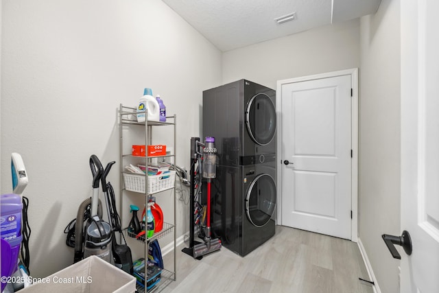 laundry room featuring light wood-type flooring, stacked washing maching and dryer, and a textured ceiling