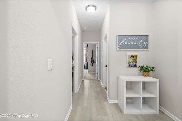 hallway with a textured ceiling and light hardwood / wood-style flooring