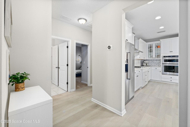 kitchen with white cabinets, stainless steel double oven, light hardwood / wood-style flooring, and tasteful backsplash