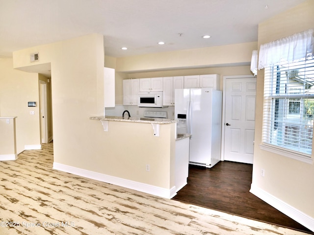 kitchen featuring white cabinets, a breakfast bar, white appliances, and light hardwood / wood-style flooring