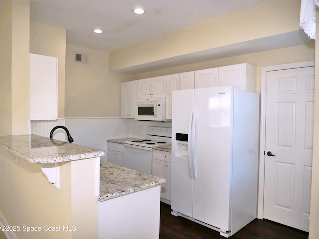 kitchen with dark wood-type flooring, kitchen peninsula, white appliances, a breakfast bar area, and white cabinets