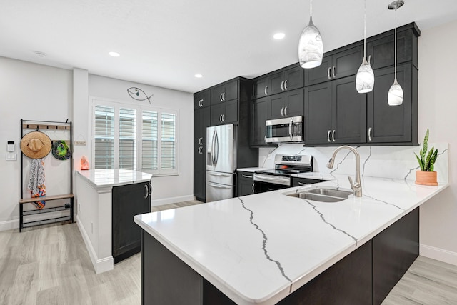 kitchen with sink, decorative light fixtures, light hardwood / wood-style floors, kitchen peninsula, and appliances with stainless steel finishes