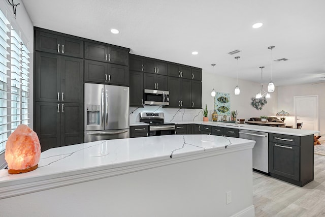 kitchen featuring light stone counters, kitchen peninsula, hanging light fixtures, light hardwood / wood-style floors, and appliances with stainless steel finishes