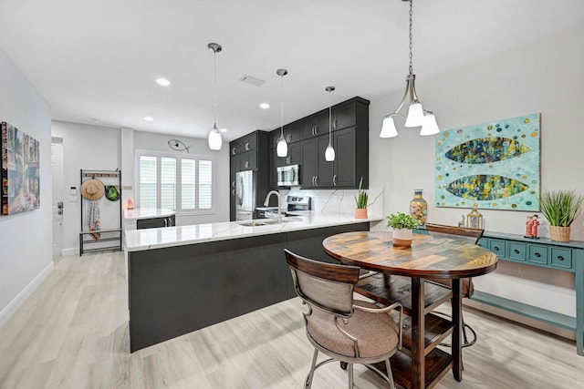 kitchen with stainless steel appliances, sink, light hardwood / wood-style flooring, kitchen peninsula, and hanging light fixtures