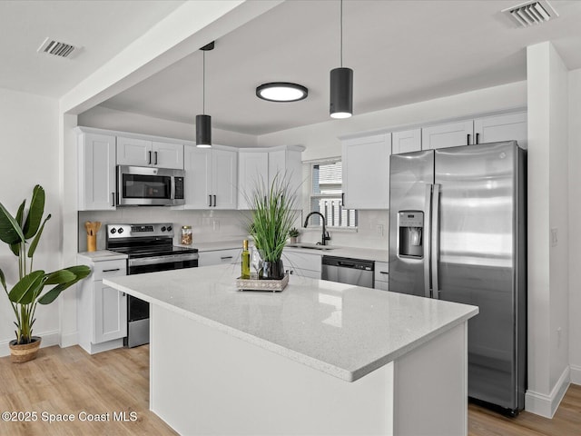 kitchen featuring white cabinets, decorative light fixtures, a center island, and stainless steel appliances