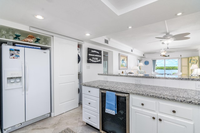 kitchen featuring ceiling fan, white fridge with ice dispenser, beverage cooler, a raised ceiling, and white cabinets