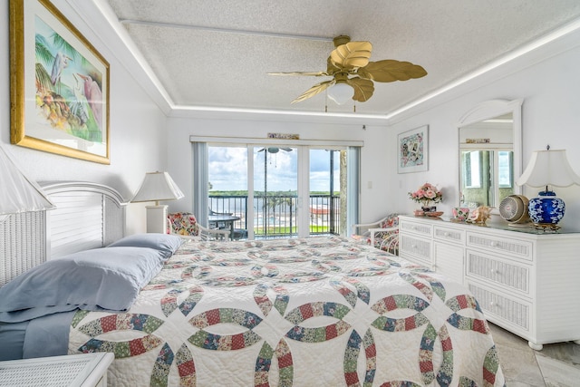 tiled bedroom with ceiling fan, access to exterior, a textured ceiling, and a tray ceiling