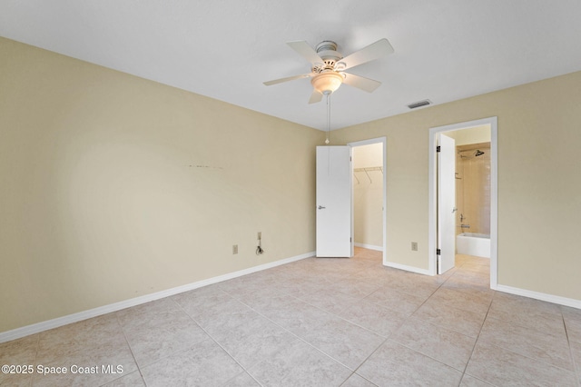 unfurnished bedroom featuring ceiling fan, light tile patterned floors, ensuite bath, a walk in closet, and a closet