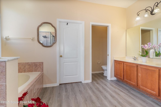 bathroom featuring hardwood / wood-style flooring, tiled bath, toilet, and vanity