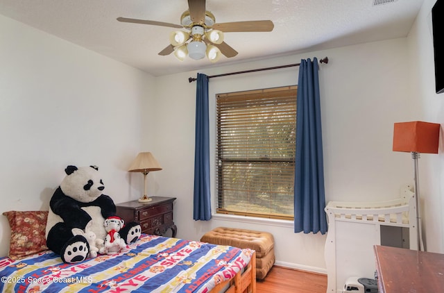 bedroom featuring a textured ceiling, ceiling fan, wood-type flooring, and multiple windows