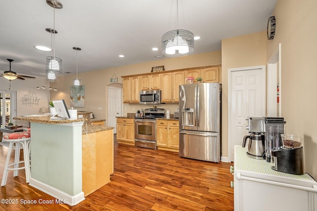 kitchen with ceiling fan, appliances with stainless steel finishes, decorative light fixtures, light stone counters, and wood-type flooring