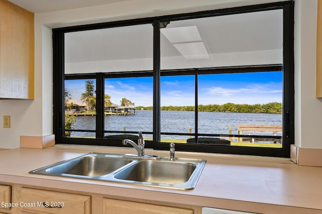 kitchen with light brown cabinets, a water view, and sink