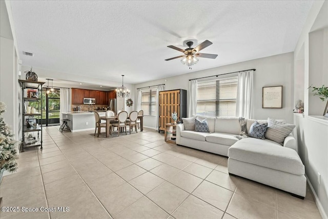 living room with ceiling fan with notable chandelier, a wealth of natural light, a textured ceiling, and light tile patterned flooring