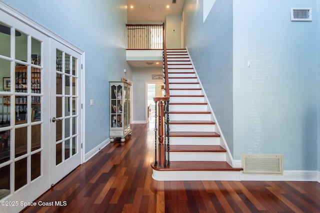 staircase with french doors, a towering ceiling, a healthy amount of sunlight, and wood-type flooring