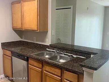 kitchen featuring stainless steel dishwasher, dark stone countertops, and sink