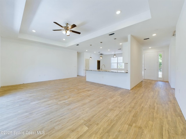 unfurnished living room featuring ceiling fan, light hardwood / wood-style floors, a raised ceiling, and sink