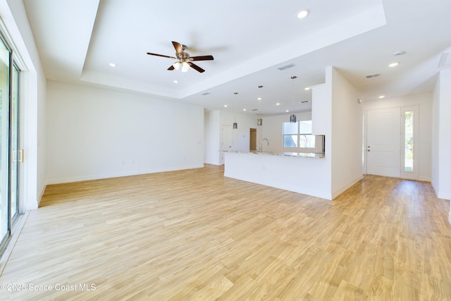 unfurnished living room featuring a tray ceiling, ceiling fan, light hardwood / wood-style flooring, and sink