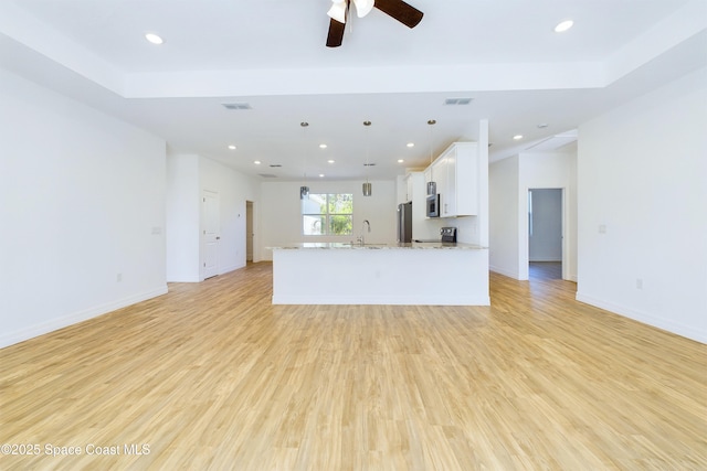 kitchen with sink, an island with sink, pendant lighting, light hardwood / wood-style floors, and white cabinets