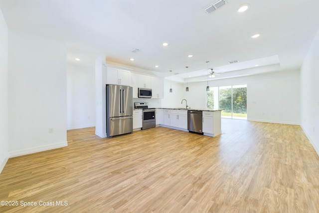 kitchen featuring appliances with stainless steel finishes, light wood-type flooring, sink, white cabinetry, and hanging light fixtures