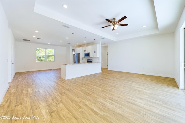 unfurnished living room featuring light wood-type flooring, a tray ceiling, and ceiling fan