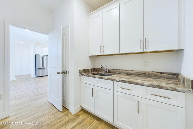 kitchen with stainless steel refrigerator, sink, dark stone countertops, light hardwood / wood-style floors, and white cabinets