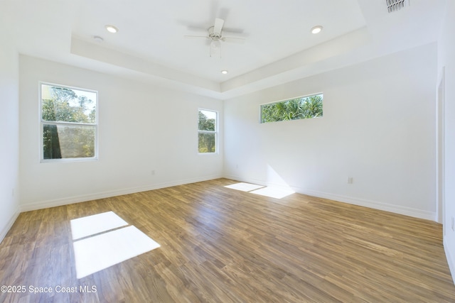 unfurnished room with ceiling fan, a raised ceiling, and wood-type flooring