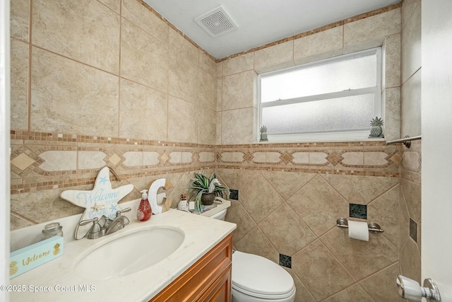 bathroom with toilet, vanity, and tile walls