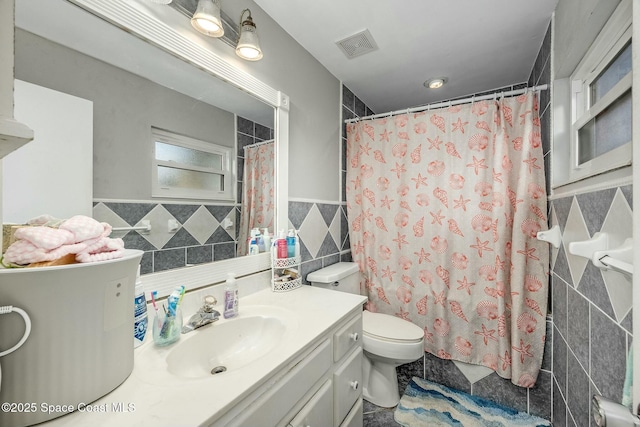 bathroom with toilet, vanity, and tile walls