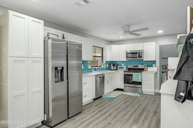 kitchen with white cabinetry, ceiling fan, appliances with stainless steel finishes, backsplash, and light wood-type flooring